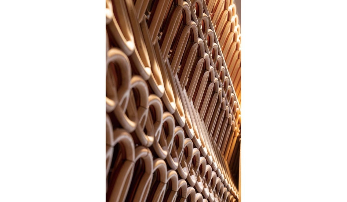 Stacked bentwood chair frames in warm honey tones, arranged diagonally to create repeating curved loops and layered wooden arches.