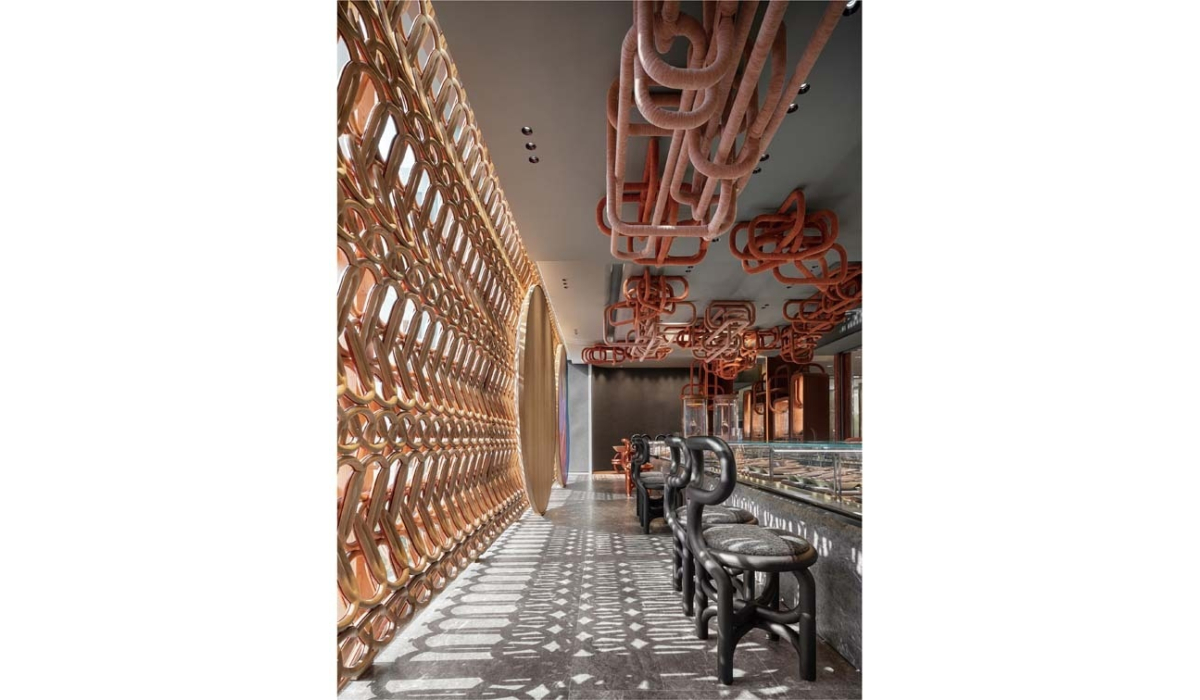 Sunlit pastry bar with a lattice gold wall casting patterned shadows, looped terracotta ceiling sculptures and black bentwood bar stools.