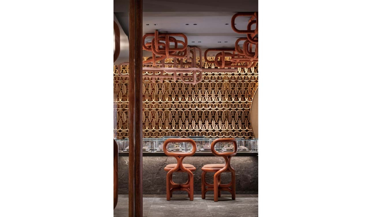 Two terracotta looped stools face a glass-topped display counter beneath an intricate wooden lattice wall and looping ceiling pipes.