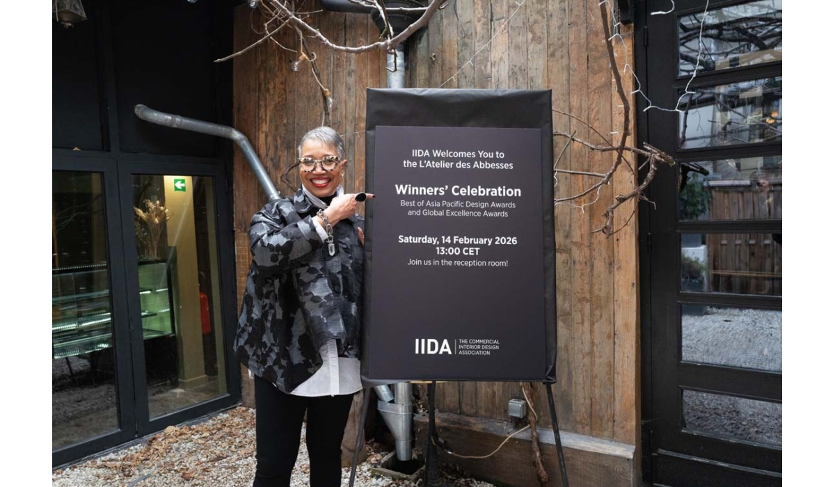 A smiling woman in a stylish outfit stands beside a sign announcing the IIDA Winners' Celebration on February 14, 2026.