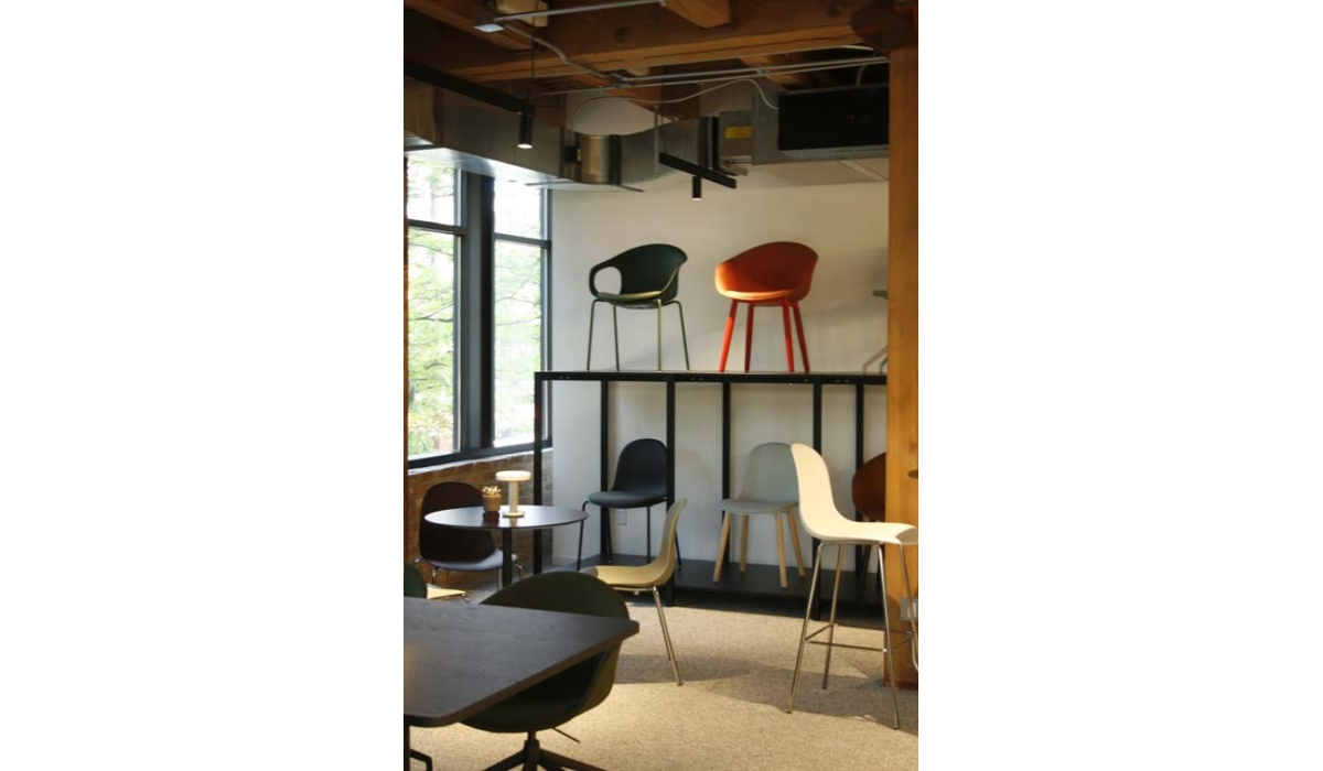 Modern furniture showroom with colorful molded chairs displayed on black shelving and arranged around tables beneath exposed wooden beams.