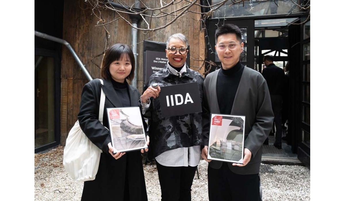 Three people stand together outside an event space, holding awards and a sign that reads "IIDA," celebrating a design achievement.