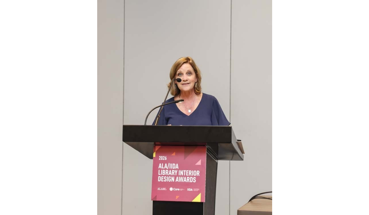 Woman with light brown hair speaks at a podium microphone above a banner reading '2026 ALA/IIDA Library Interior Design Awards.'