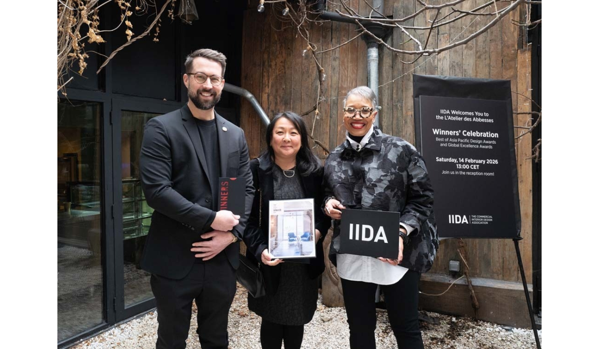 Three individuals stand together, celebrating as winners in front of a wooden backdrop, with event signage for the IIDA's awards.