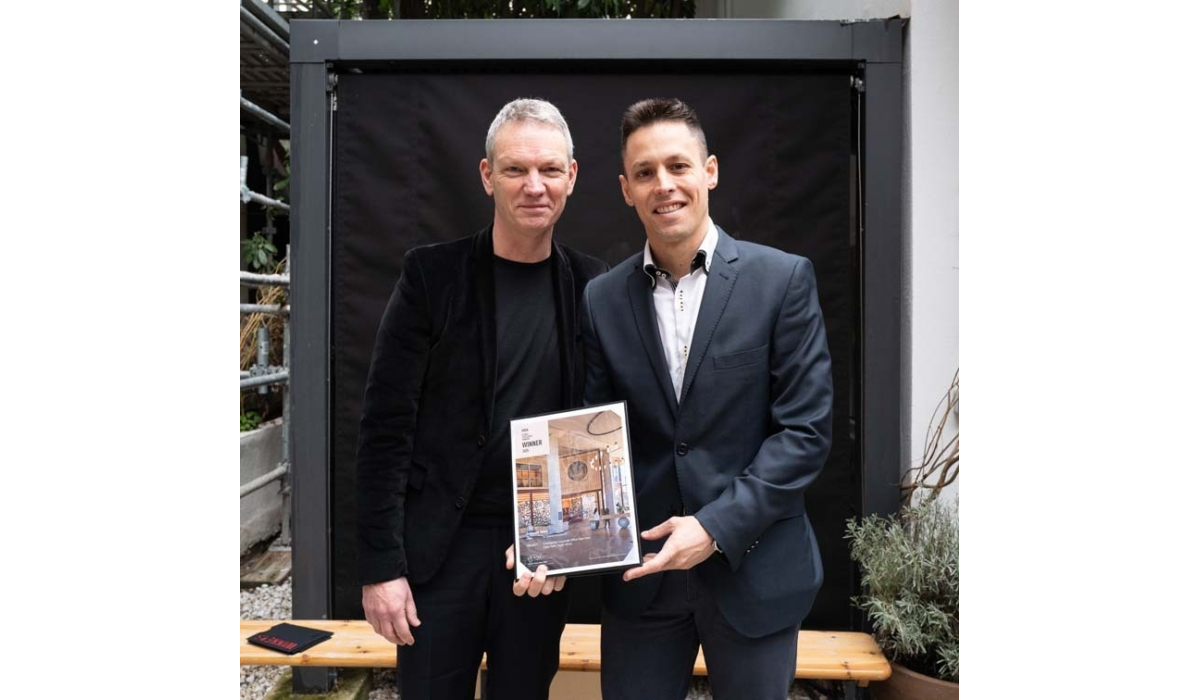 Two men stand together, both smiling, holding a booklet titled "Winner," showcasing an elegant interior design.