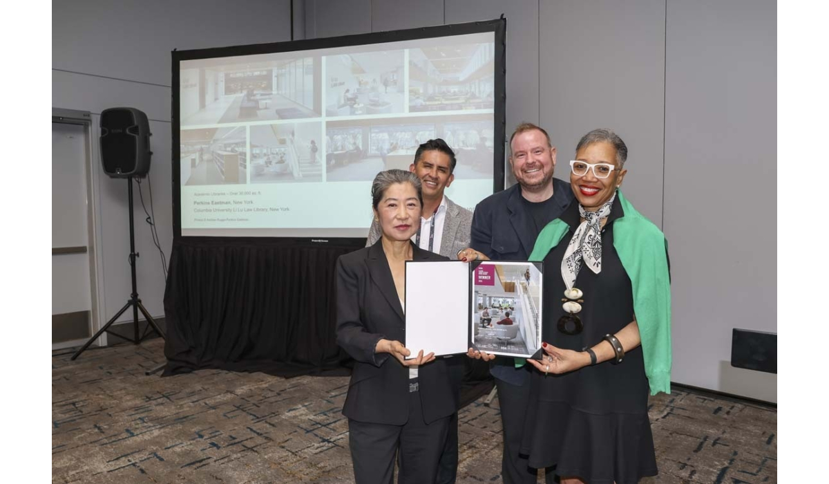 Four colleagues standing before a projector screen in a conference room, smiling and holding a framed award certificate together.