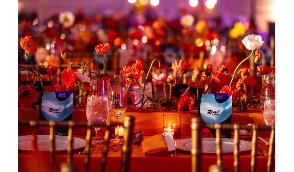 Dinner table with vibrant red poppy centerpieces, glowing votive candles, wine glasses, plates and award cards beneath warm ambient lights.