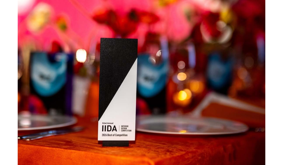 Black-and-white IIDA 52nd award labeled 2026 Best of Competition on an orange velvet table, with blurred plates, glasses and red bokeh.