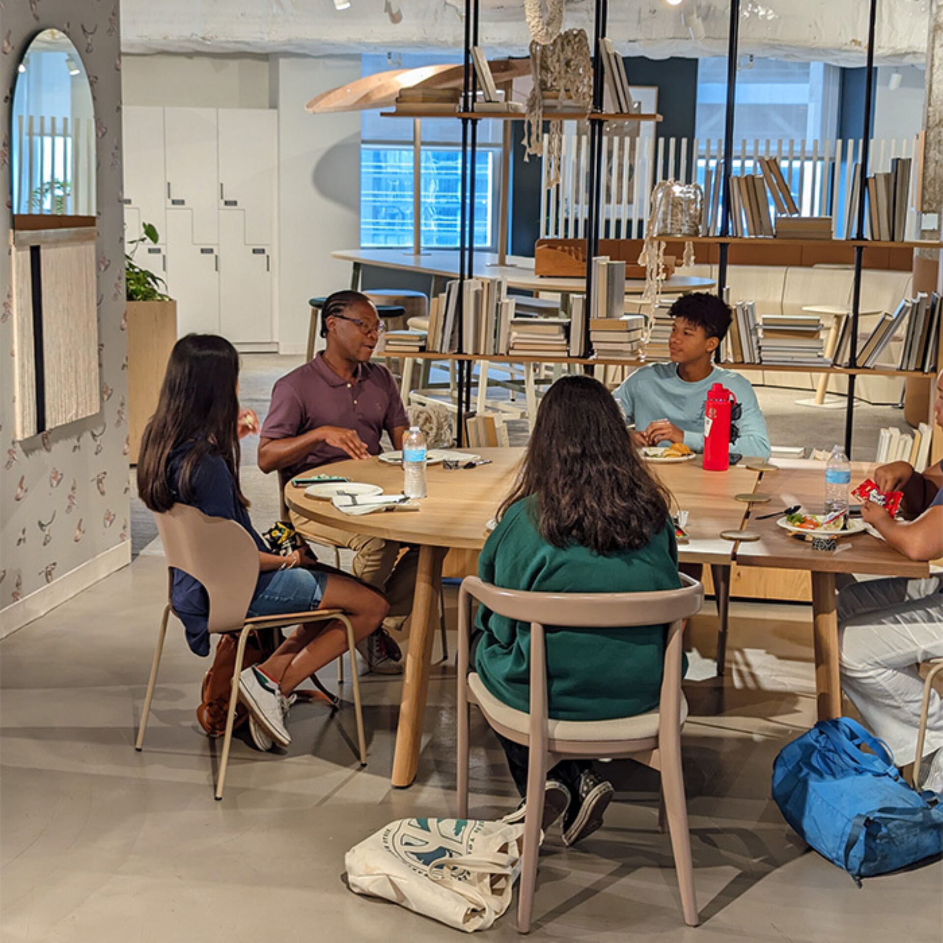 A group of five young individuals engage in conversation around a circular table in a modern, well-lit space.