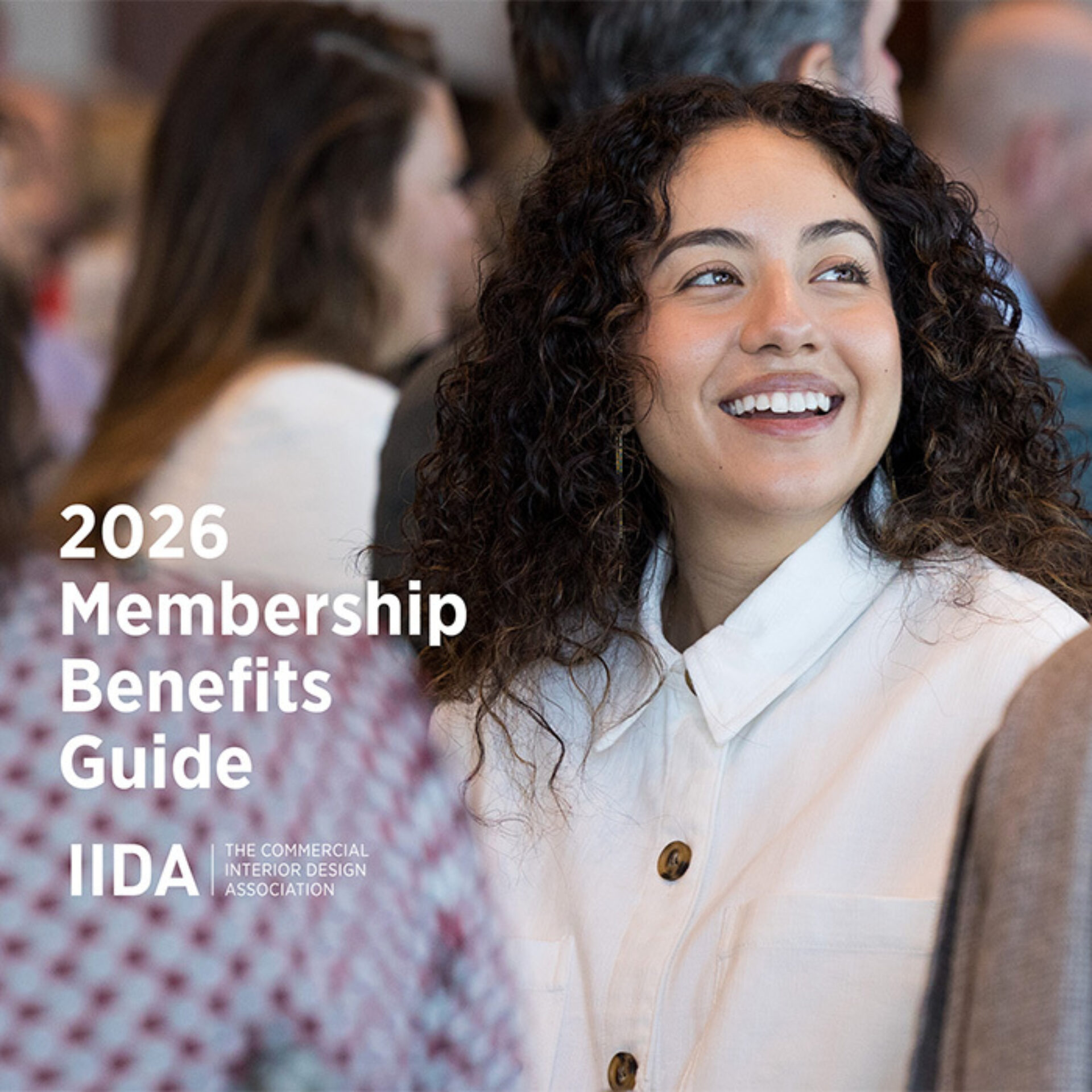 Young woman with curly hair and white buttoned shirt smiles while attendees mingle, left text reads 2026 Membership Benefits Guide.