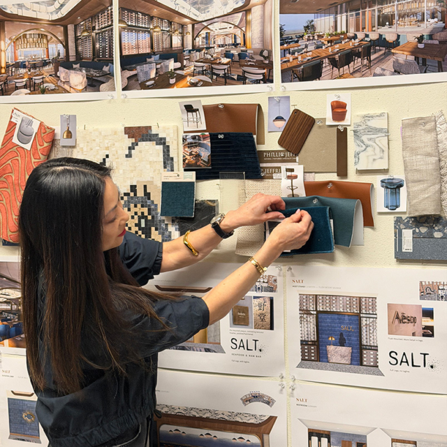 A designer arranges fabric samples and materials on a wall filled with various design inspirations and concept images for a project.