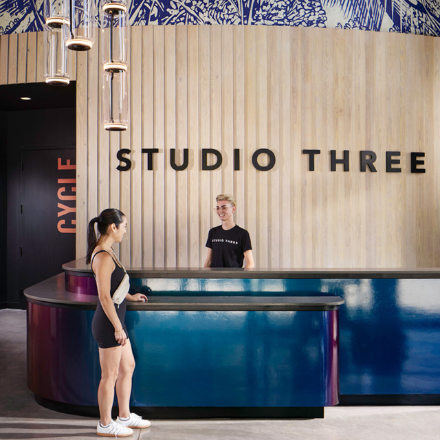 A welcoming reception area at Studio Three features a stylish curved counter, where a staff member assists a client.