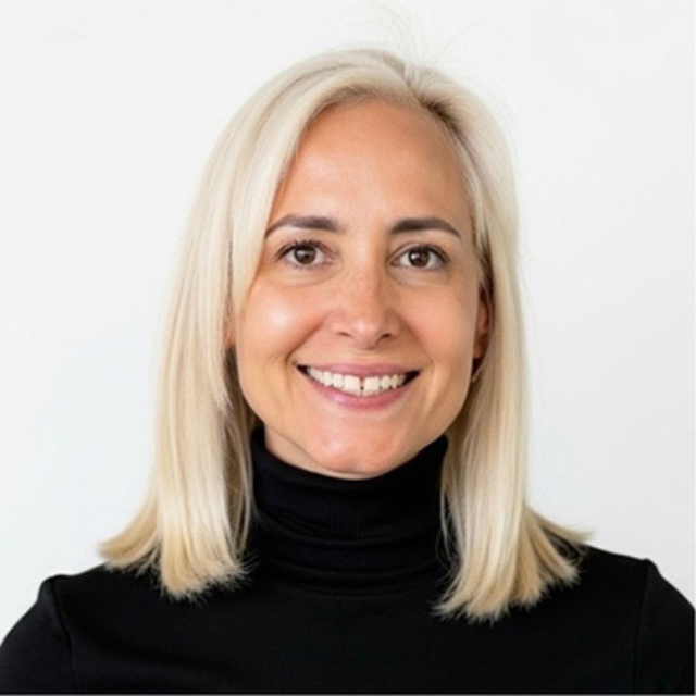 Smiling woman with shoulder-length platinum blonde hair, wearing a black turtleneck, neutral background and a warm expression.