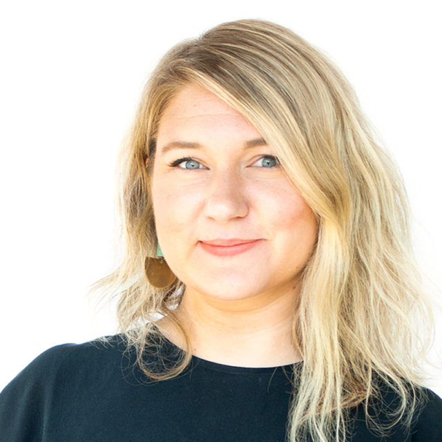 A woman with wavy blonde hair and blue eyes wears a black shirt and dangling earrings, smiling against a white background.