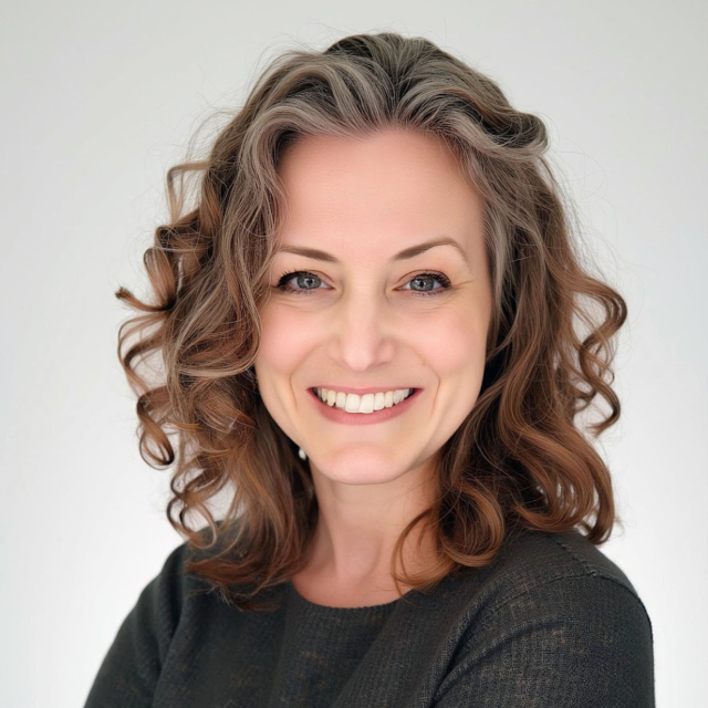A woman with curly, shoulder-length hair smiles warmly, wearing a dark sweater against a light background. Her expression is friendly and approachable.