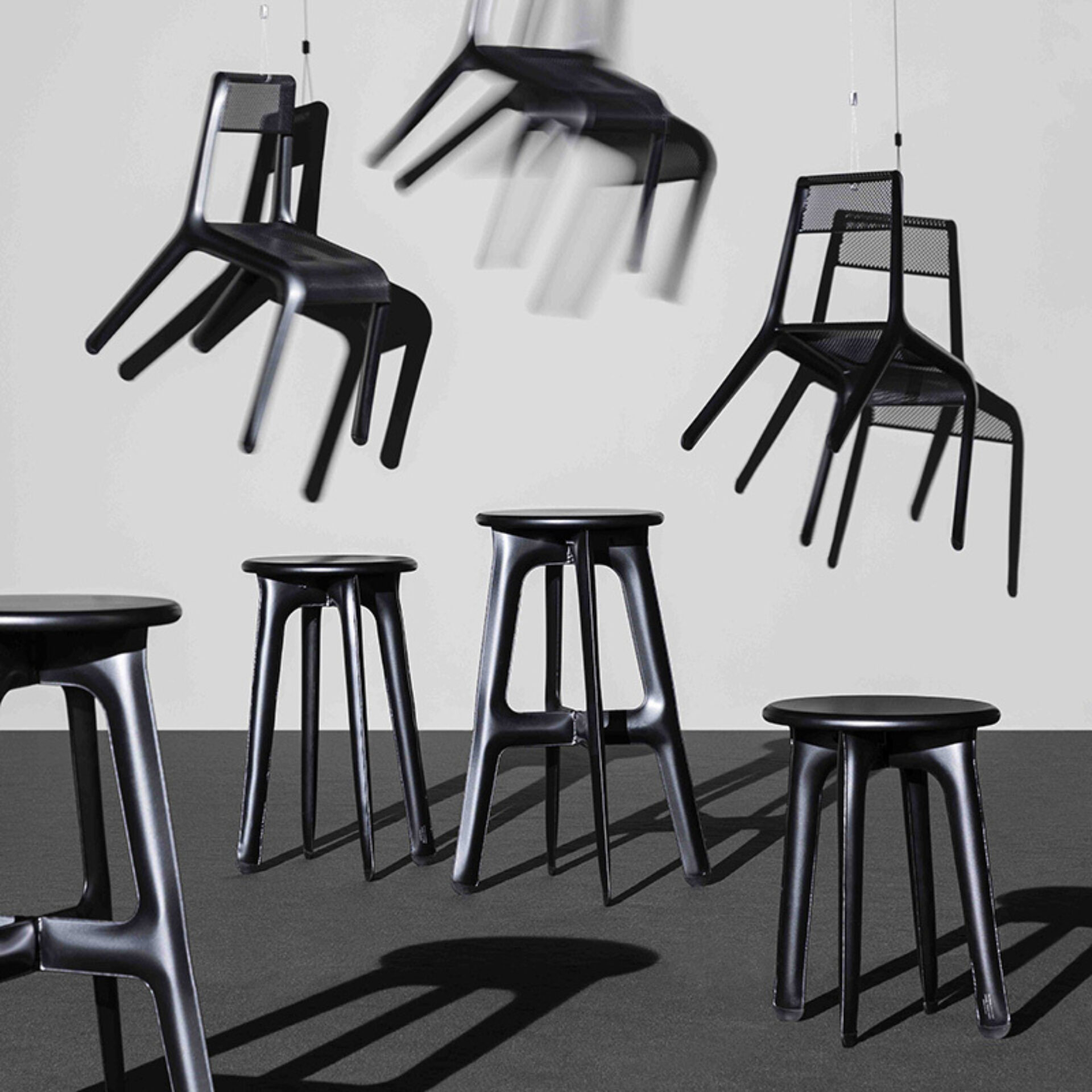 Black chairs are suspended in mid-air above a group of black stools on a dark floor, showcasing a modern and minimalist design.