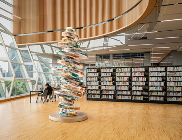 A modern library interior featuring a spiral sculpture and shelves filled with books, complemented by large windows and natural light.