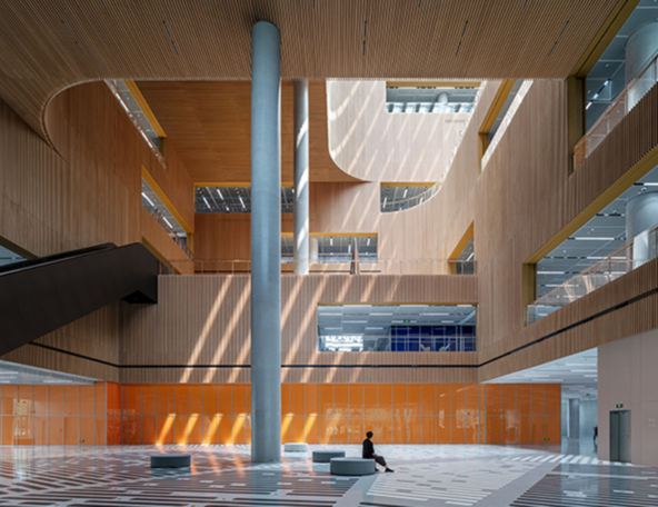 A modern architectural interior features warm wooden accents and large glass windows, with sharp light contrasts and a lone figure seated.