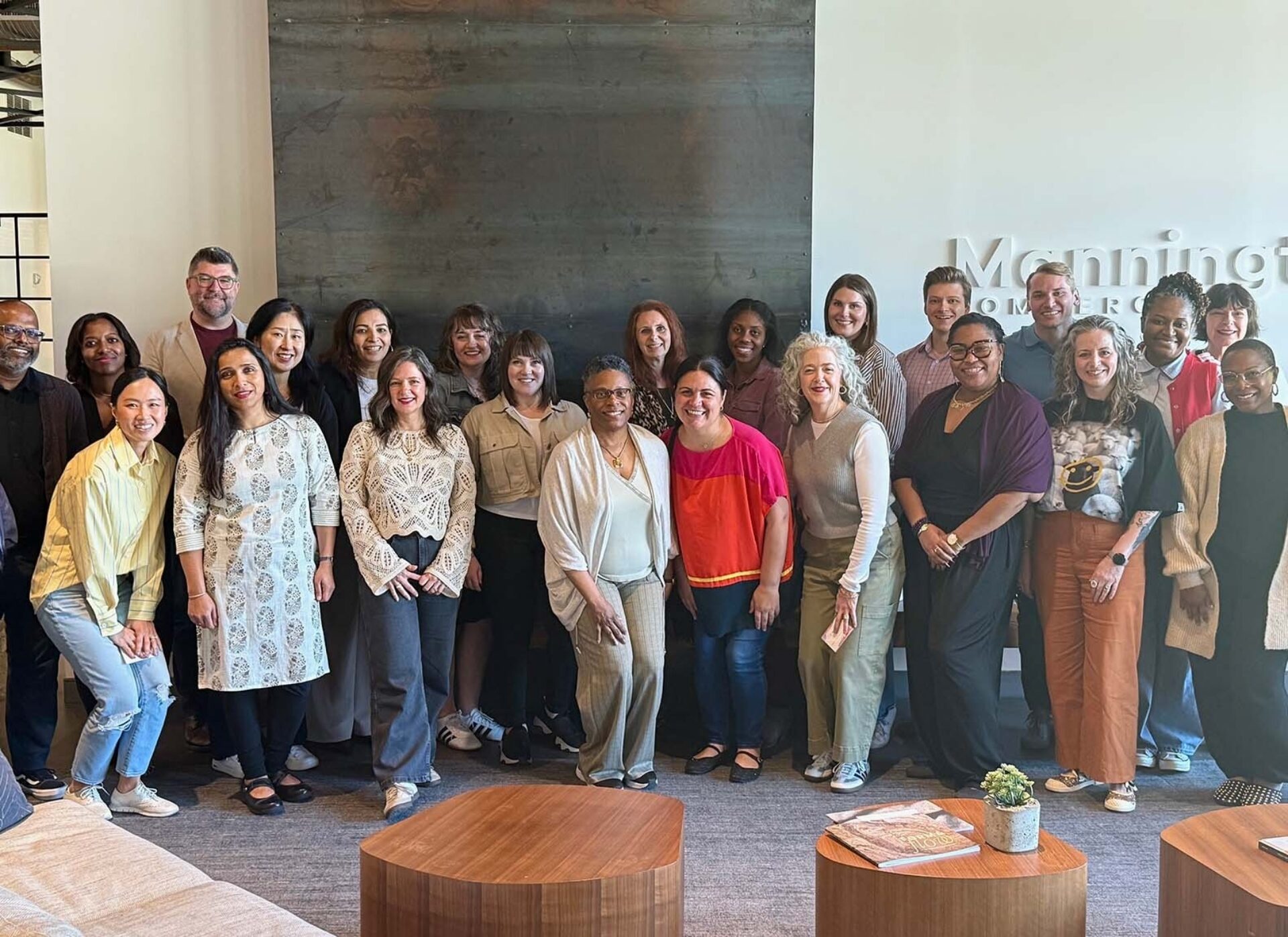 A diverse group of colleagues stands together in a bright office space, smiling for a photo, showcasing teamwork and collaboration.
