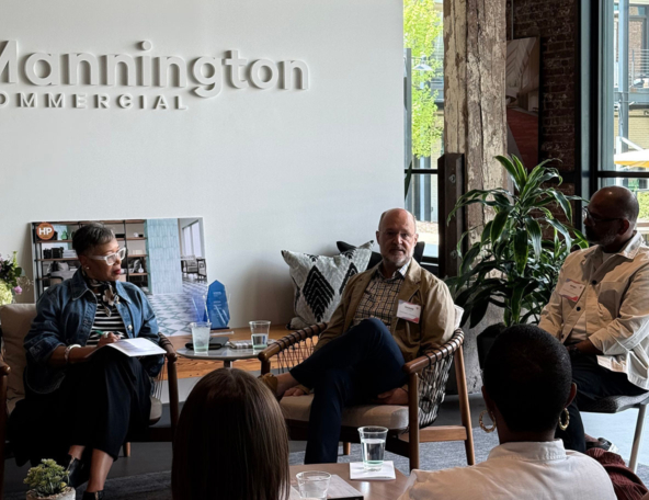 Three people participate in a panel discussion at Mannington Commercial, surrounded by plants and modern decor, engaging with the audience.