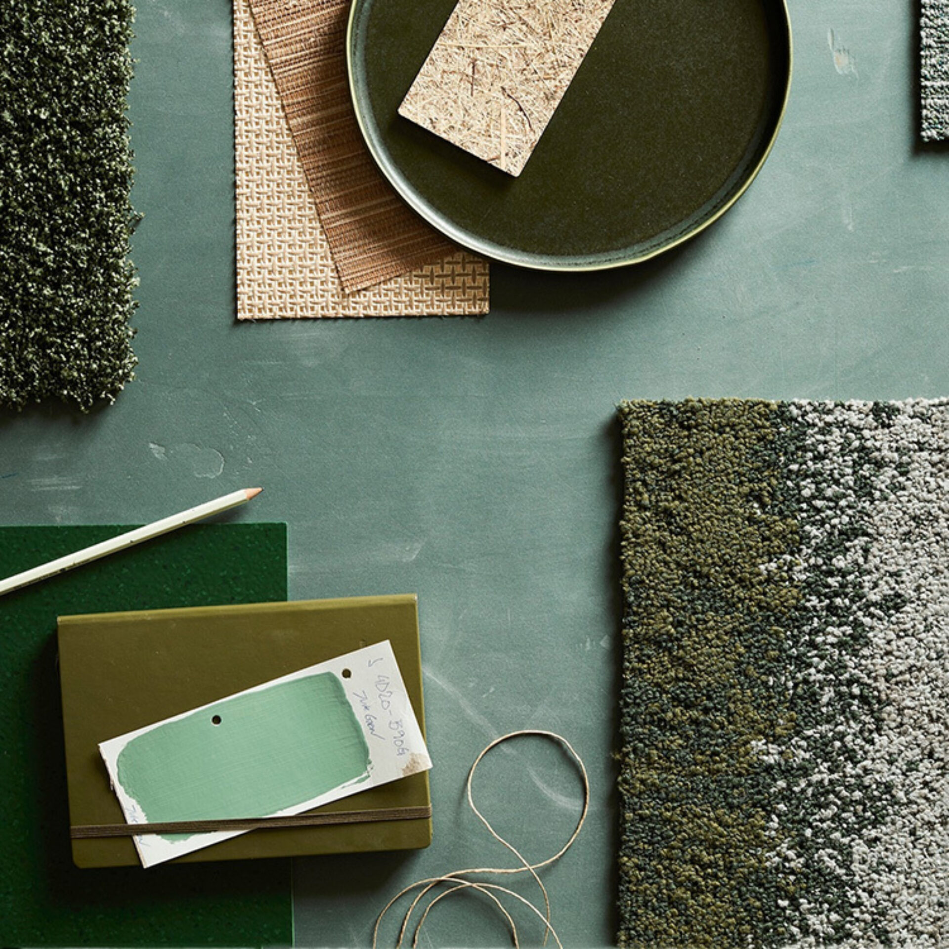 A collection of textured materials, color samples, a notebook, and a pencil arranged over a green surface, showcasing design elements.