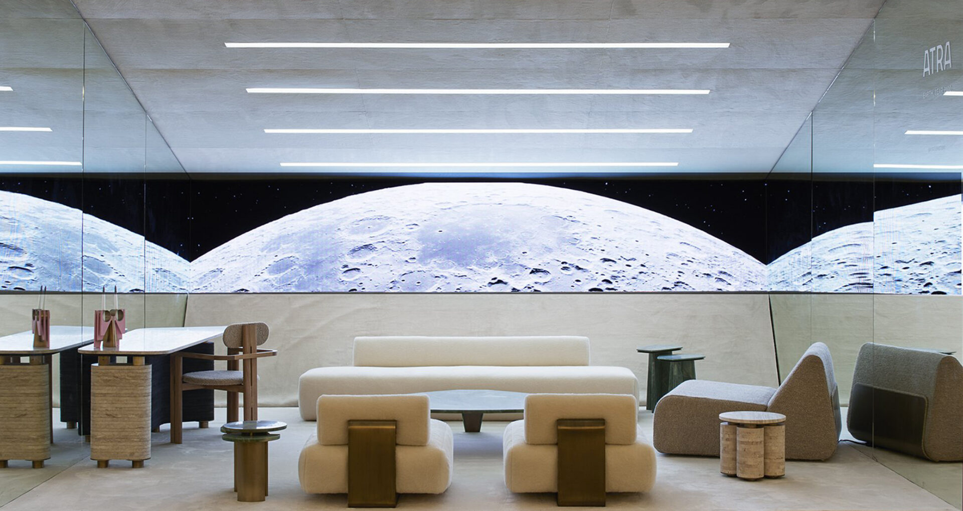 A modern, minimalist interior features plush seating, a sleek table, and a large screen displaying a lunar landscape against a dark starry backdrop.