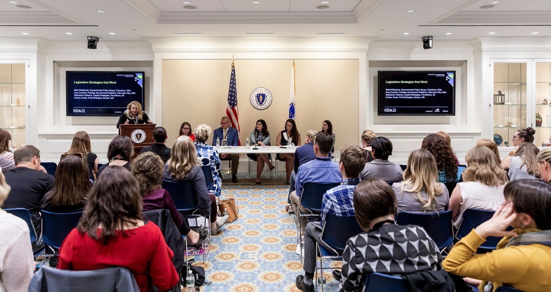 A panel discussion titled "Legislative Strategies that Work" occurs in a formal setting with audience members engaged attentively.