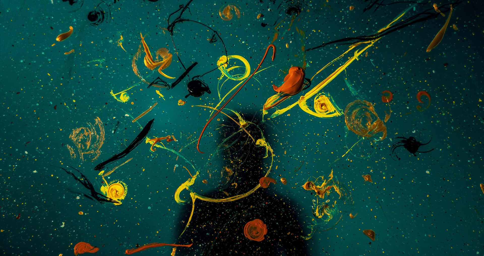 A dark background is filled with swirling, vibrant paint splatters in yellow, orange, and black, creating a dynamic, artistic scene.