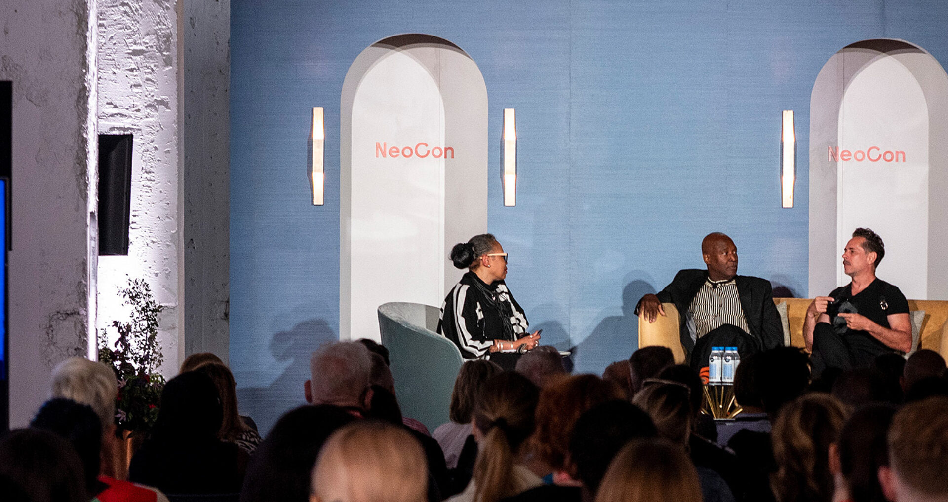A panel discussion at NeoCon features three speakers on stage, engaging the audience with insights on design and innovation.