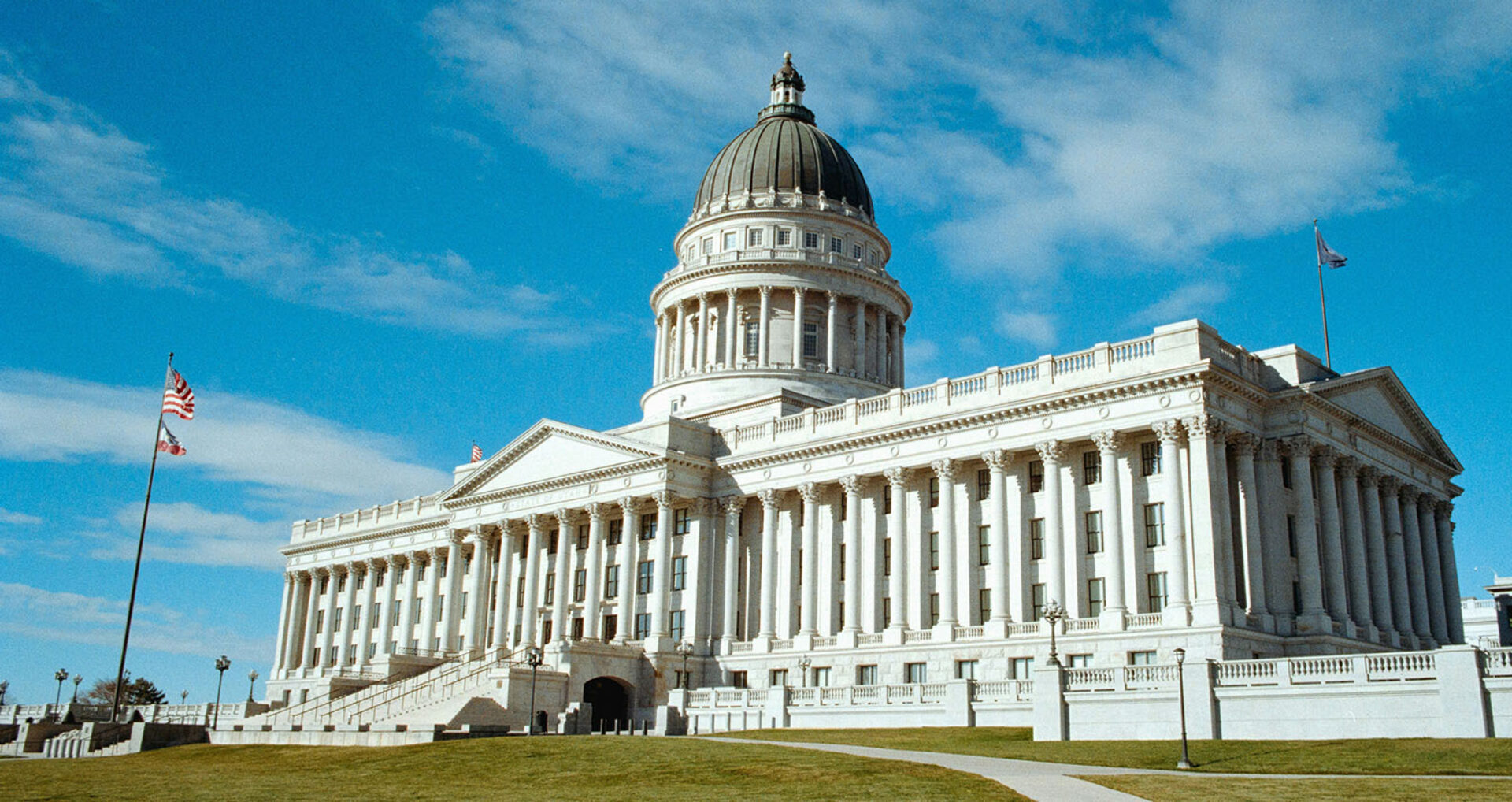 The iconic white stone building features a large dome and classical architecture, flanked by flags against a clear blue sky.