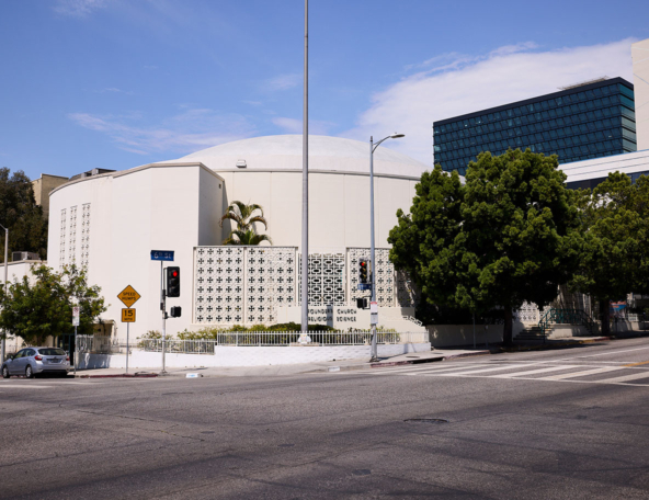 A round white building with decorative elements, surrounded by trees, traffic signals, and signs, conveys a serene urban setting.