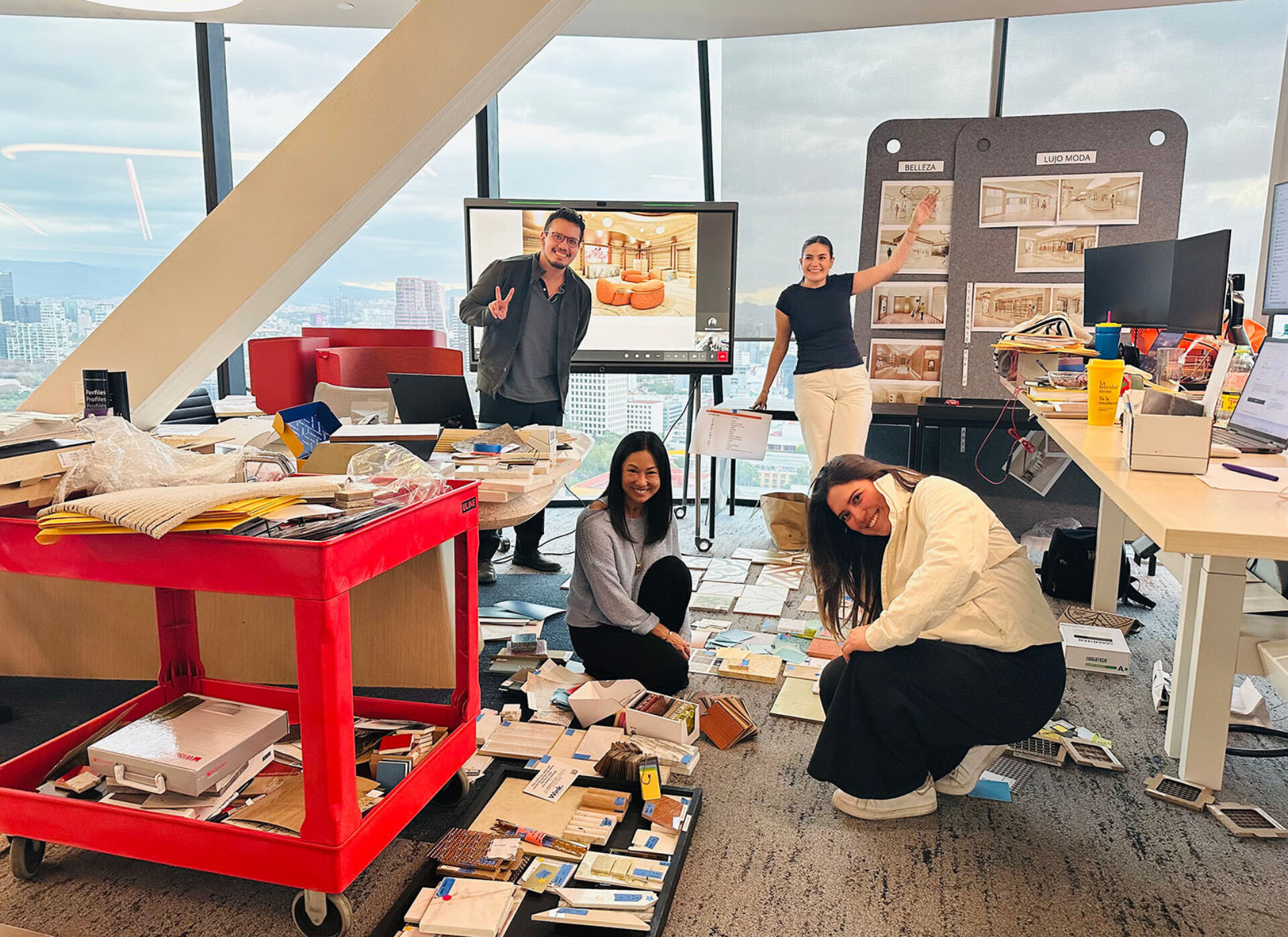 A group of four colleagues collaborates in an office filled with design materials, showcasing creativity amidst a cluttered workspace.