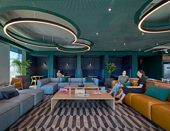 A modern lounge area features stylish seating in various colors, a coffee table with board games, and unique circular lighting above.