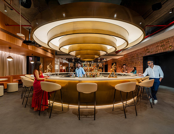 A modern bar features a circular design with soft lighting. Several patrons enjoy drinks while seated on stylish stools, creating a vibrant atmosphere.