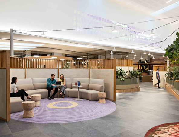 Modern workspace featuring comfortable seating, people engaged in conversation, lush plants, and creative decor elements throughout.