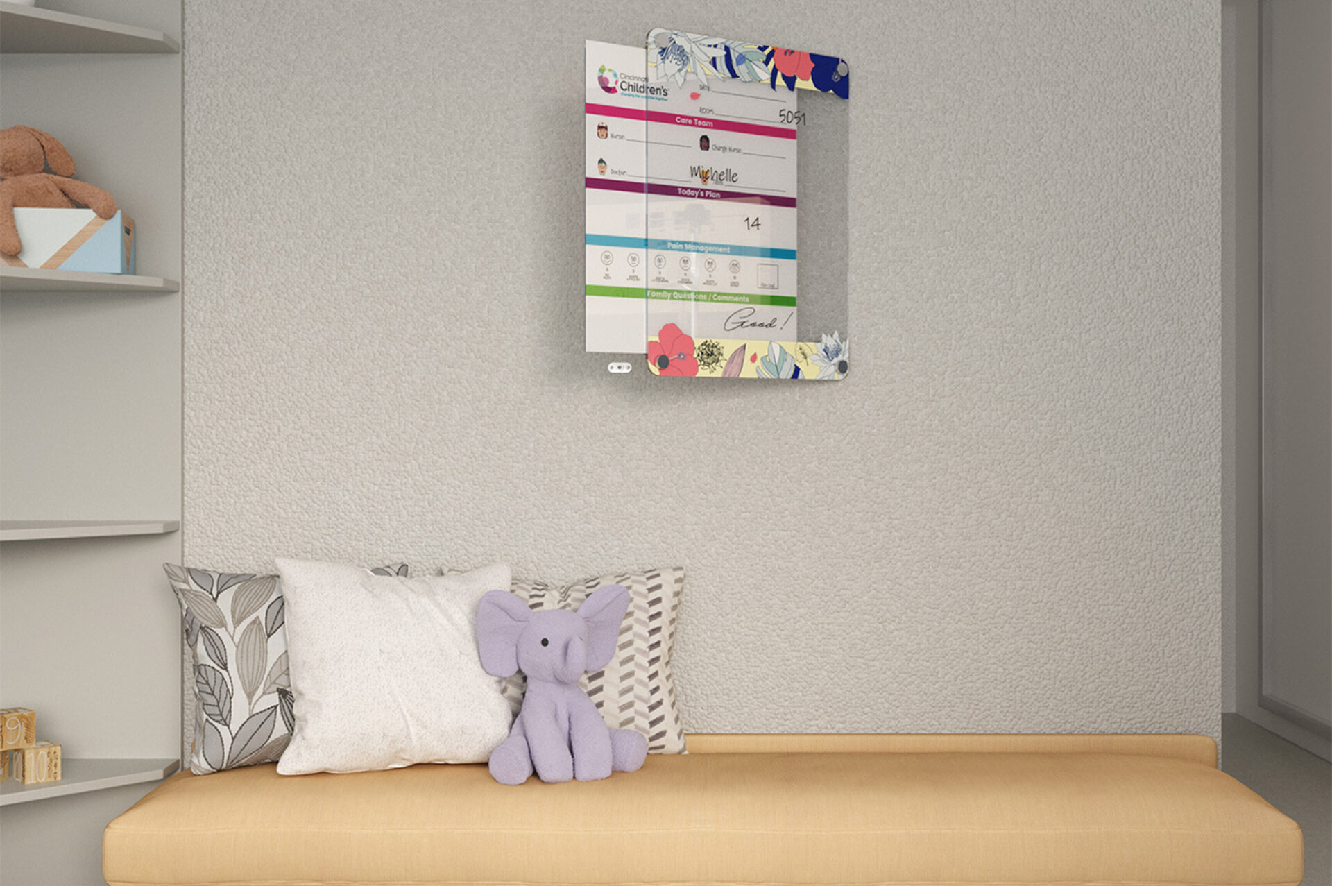 Cozy pediatric bench with patterned pillows and a small purple elephant plush, shelves holding a teddy and blocks, colorful whiteboard.