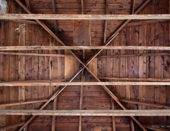 Wooden beams form an intricate pattern against a rustic ceiling, showcasing rich textures and colors of aged wood.