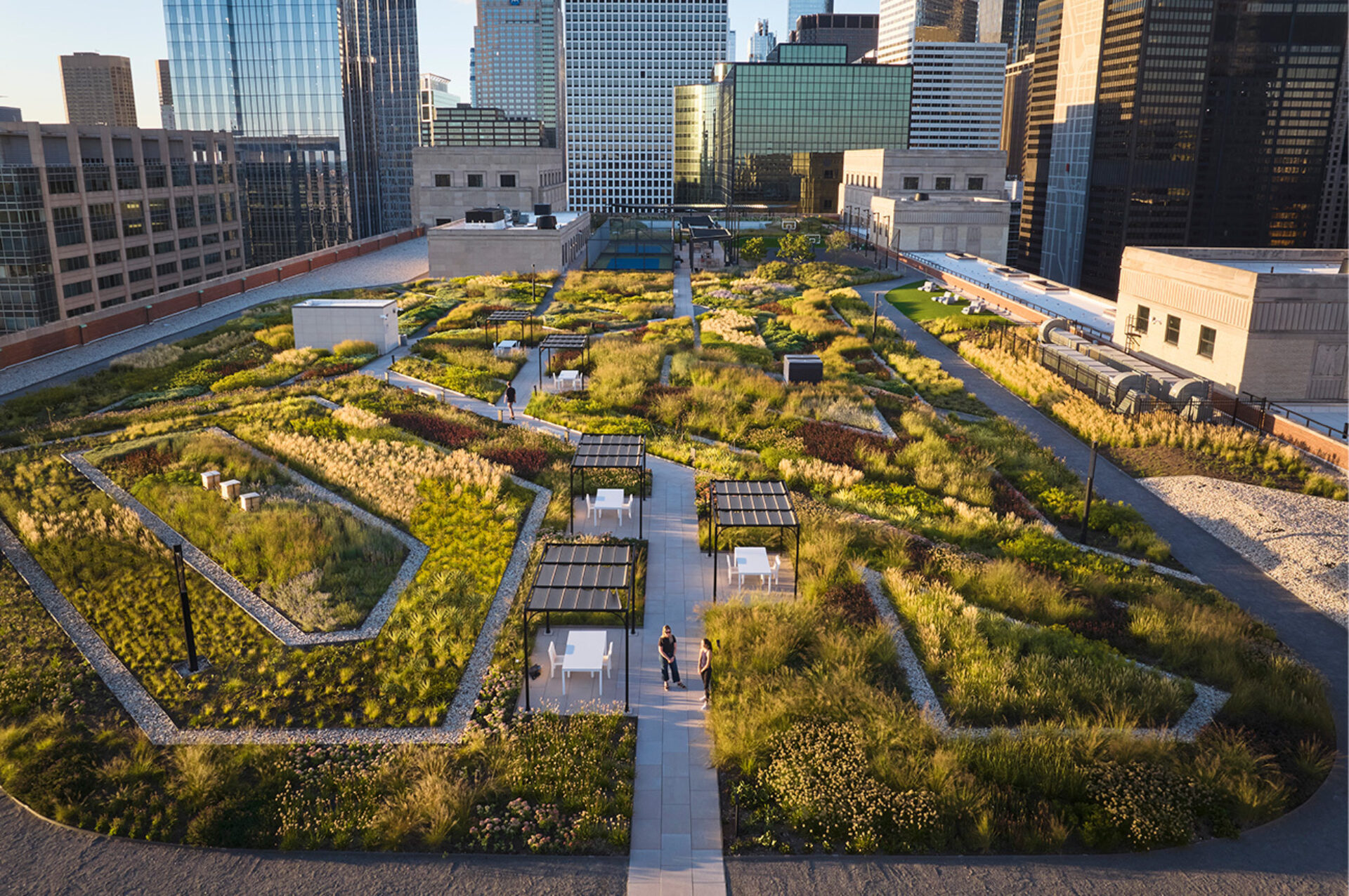 A rooftop garden features lush greenery, walking paths, seating areas, and city skyline views, inviting relaxation and exploration.