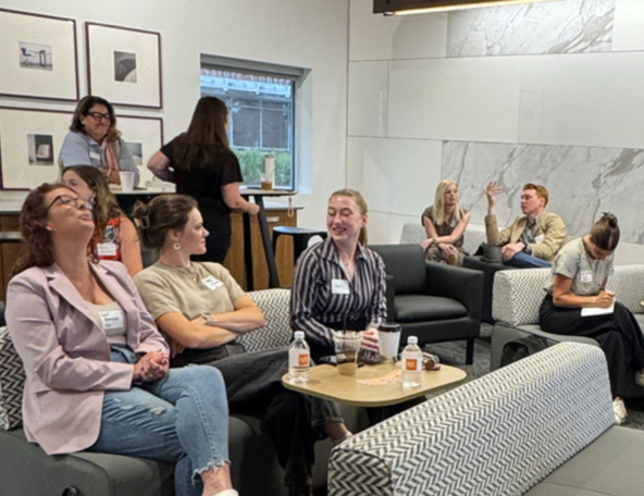 A group of people engaged in conversation in a modern lounge setting, featuring sofas and artwork, creating a dynamic atmosphere.