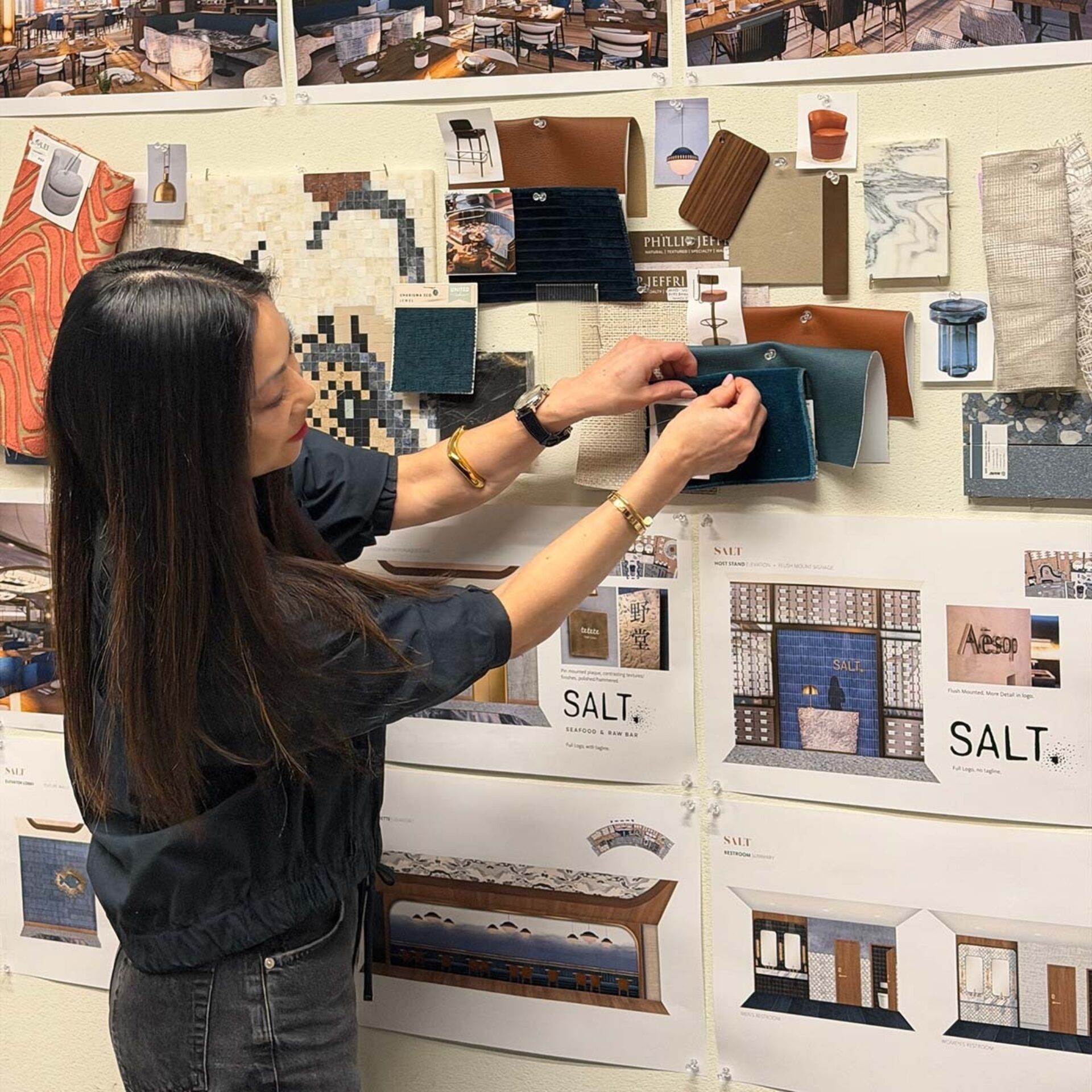 A designer organizes various fabric swatches and design renderings on a wall board, showcasing a creative workspace for a project.