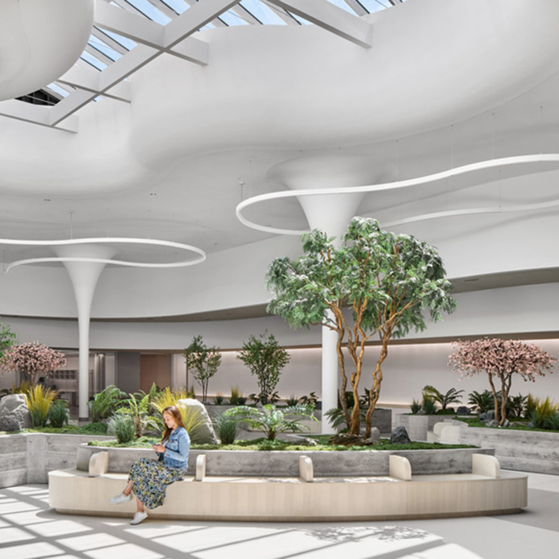 A bright, modern indoor space features a woman sitting on a curved bench amidst lush greenery and planters under a skylight.