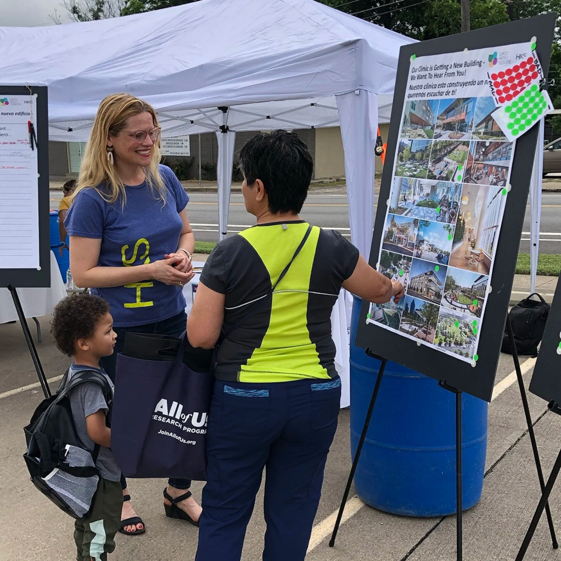 A woman with glasses engages with another woman near a display board featuring images and information about a new building project.