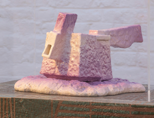 A sculptural piece featuring a textured, abstract form in pastel pink and white, displayed on a patterned surface.