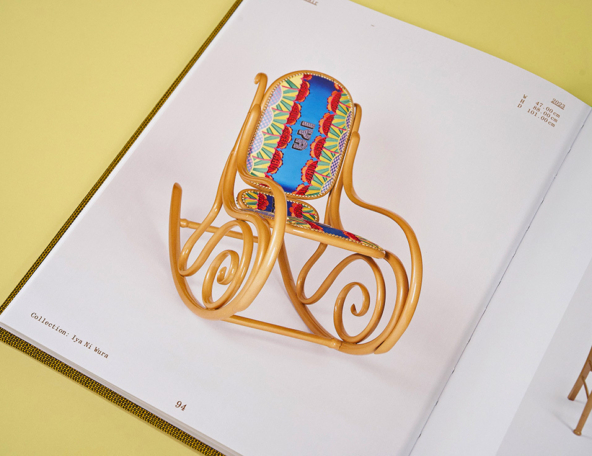 Open catalog page showing a miniature bentwood rocking chair with looping scroll arms and vibrant blue, red and yellow patterned upholstery.