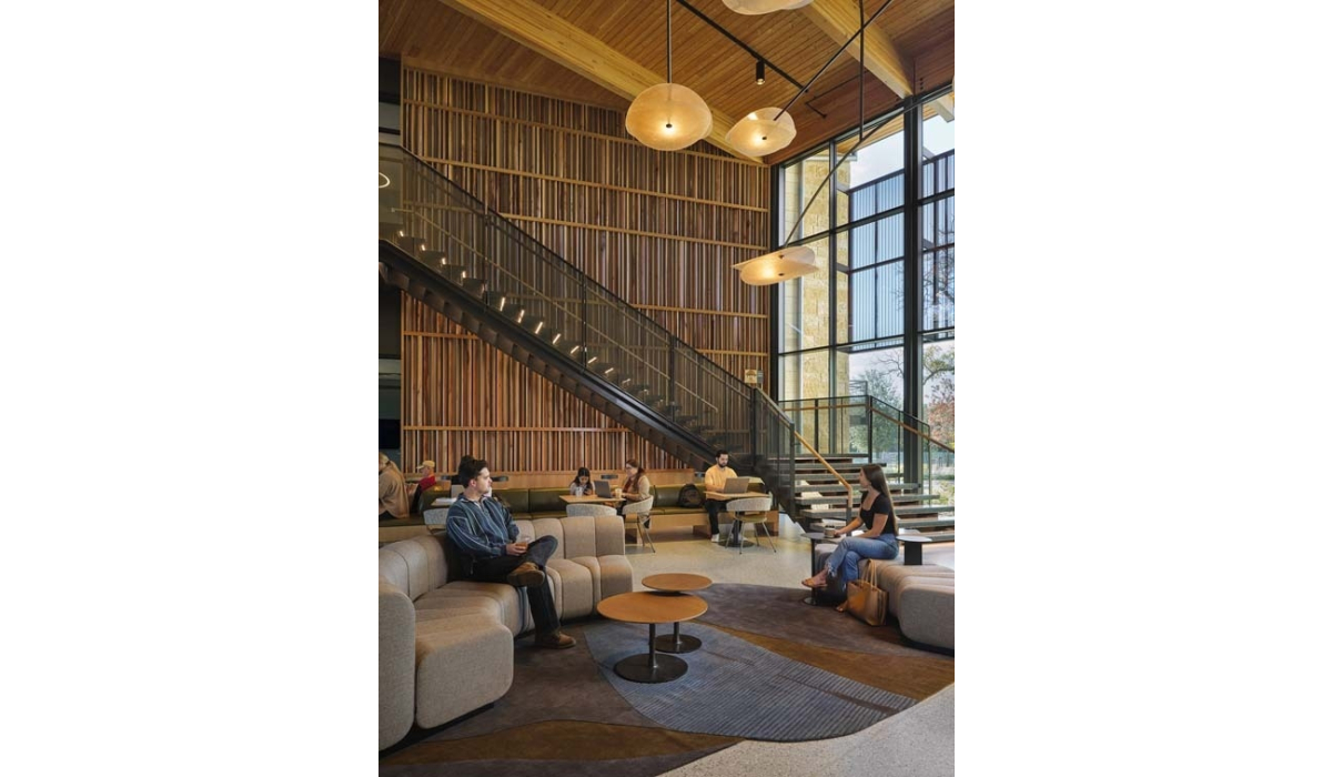 Contemporary study lounge with tall slatted wood wall, hanging round lights, glass staircase, large windows and people on sofas.