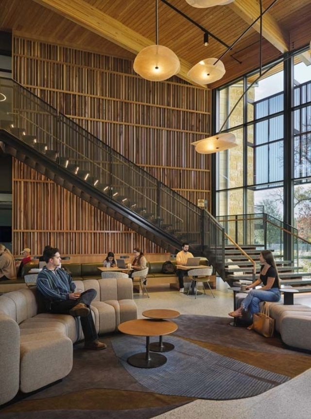 Contemporary study lounge with tall slatted wood wall, hanging round lights, glass staircase, large windows and people on sofas.