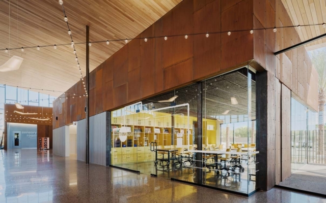 Sunlit lobby with vaulted wood ceiling, string lights and rusted metal wall; glass-walled yellow THINKspot classroom with tables and chairs.