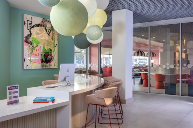 TechHub reception with curved white desk, bar stools, pastel globe pendant lights, abstract graffiti canvas and glass lounge.