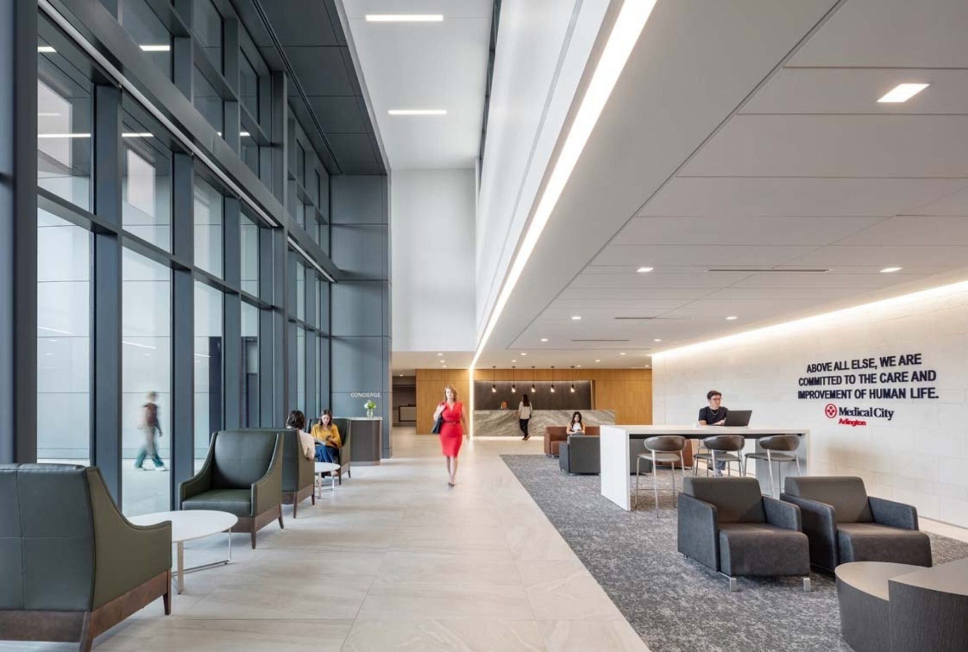 Bright hospital lobby with tall glass, concierge, seating clusters, someone in red walking toward reception under a Medical City wall sign.