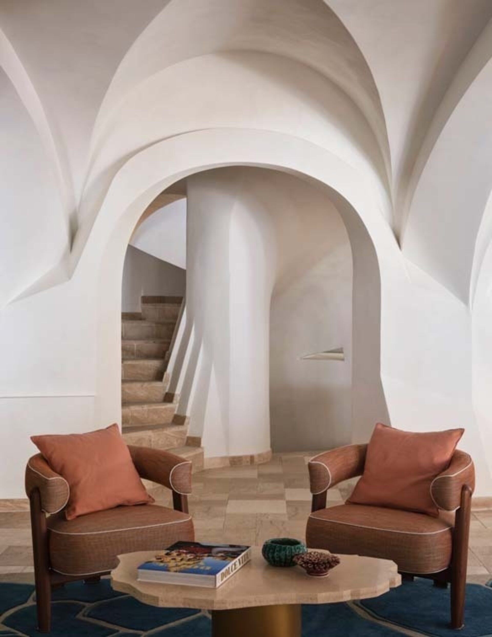 Stylish living area featuring two armchairs with cushions, a round coffee table, and a staircase leading to an arched hallway.